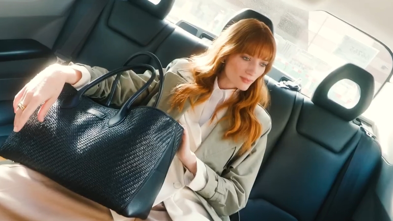 Poslovna žena sedi na zadnjem sedištu automobila i drži veliku crnu kožnu torbu elegantnog dizajna