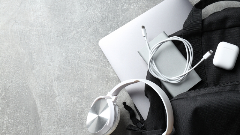 Otvoren ranac sa laptopom, punjačem i slušalicama na svetloj podlozi